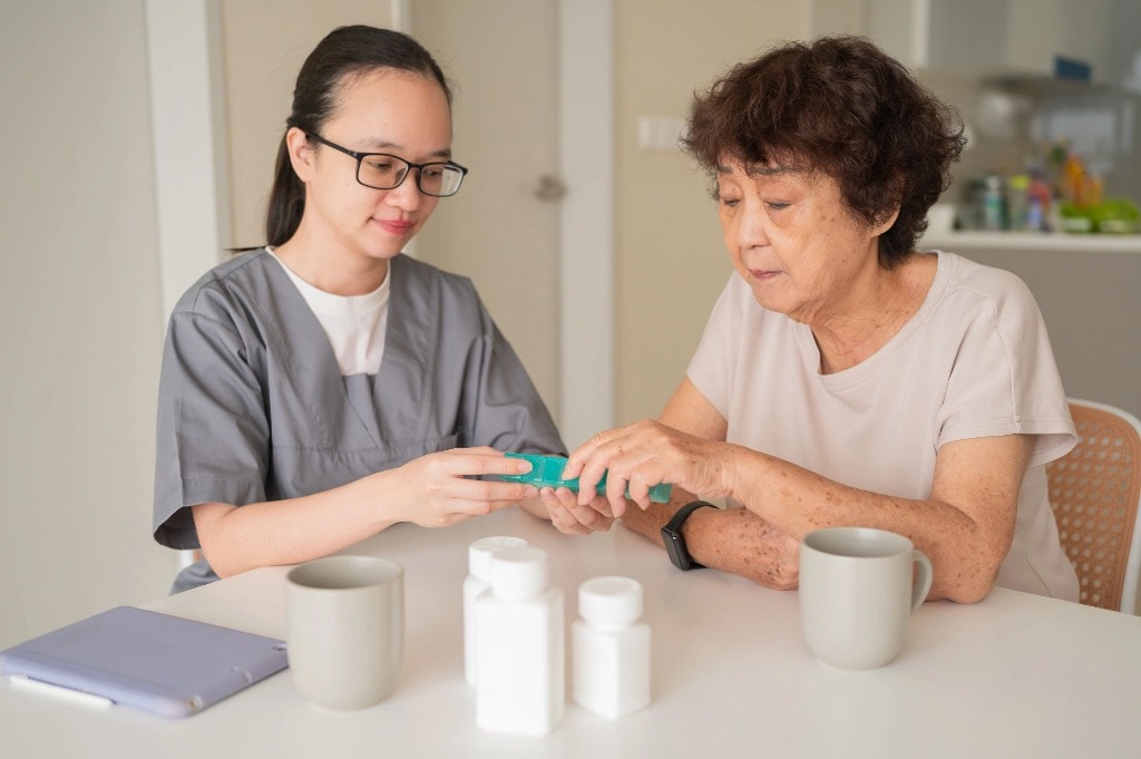 Nurse reviewing weekly pill organizer with elderly patient at home